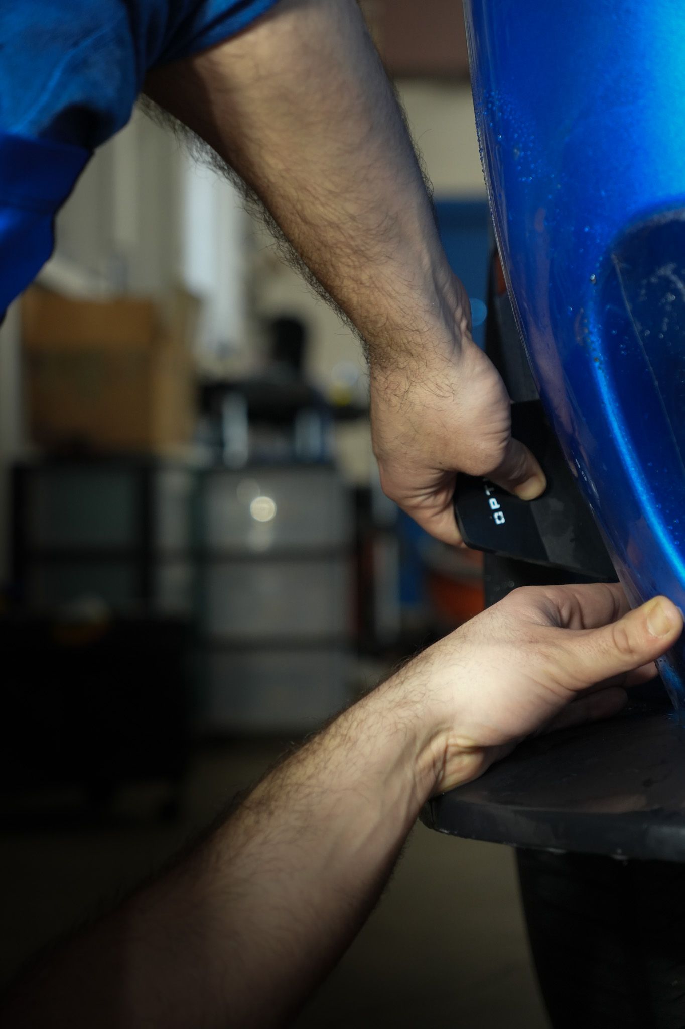 A man is working on a blue car in a garage.