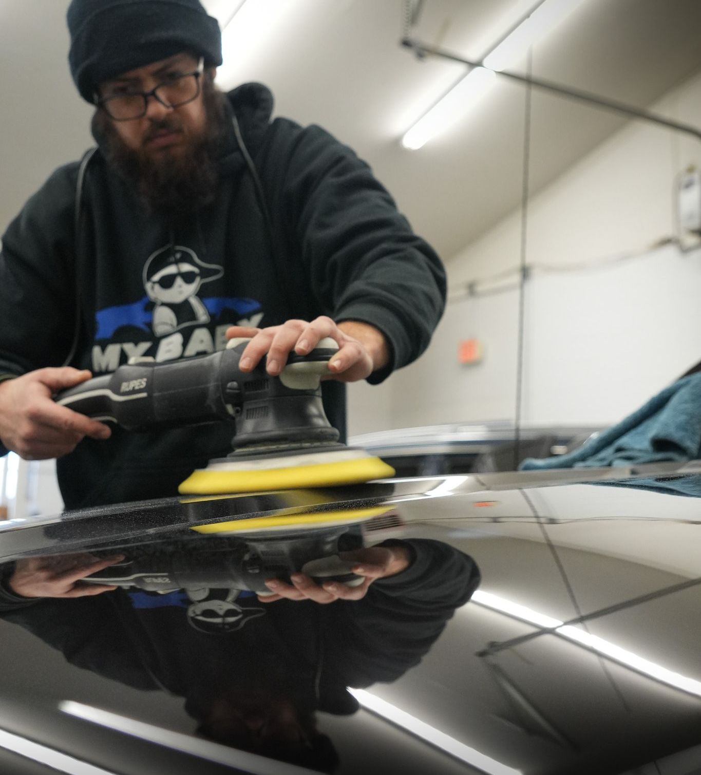 A person is polishing a car bumper with a machine.