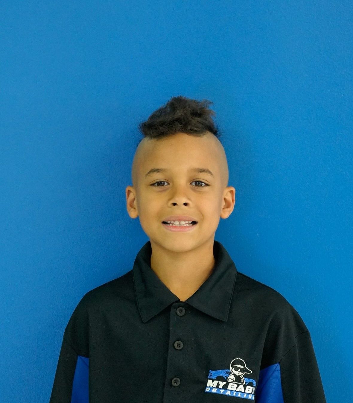 Young boy with mohawk smiling in front of a blue background.