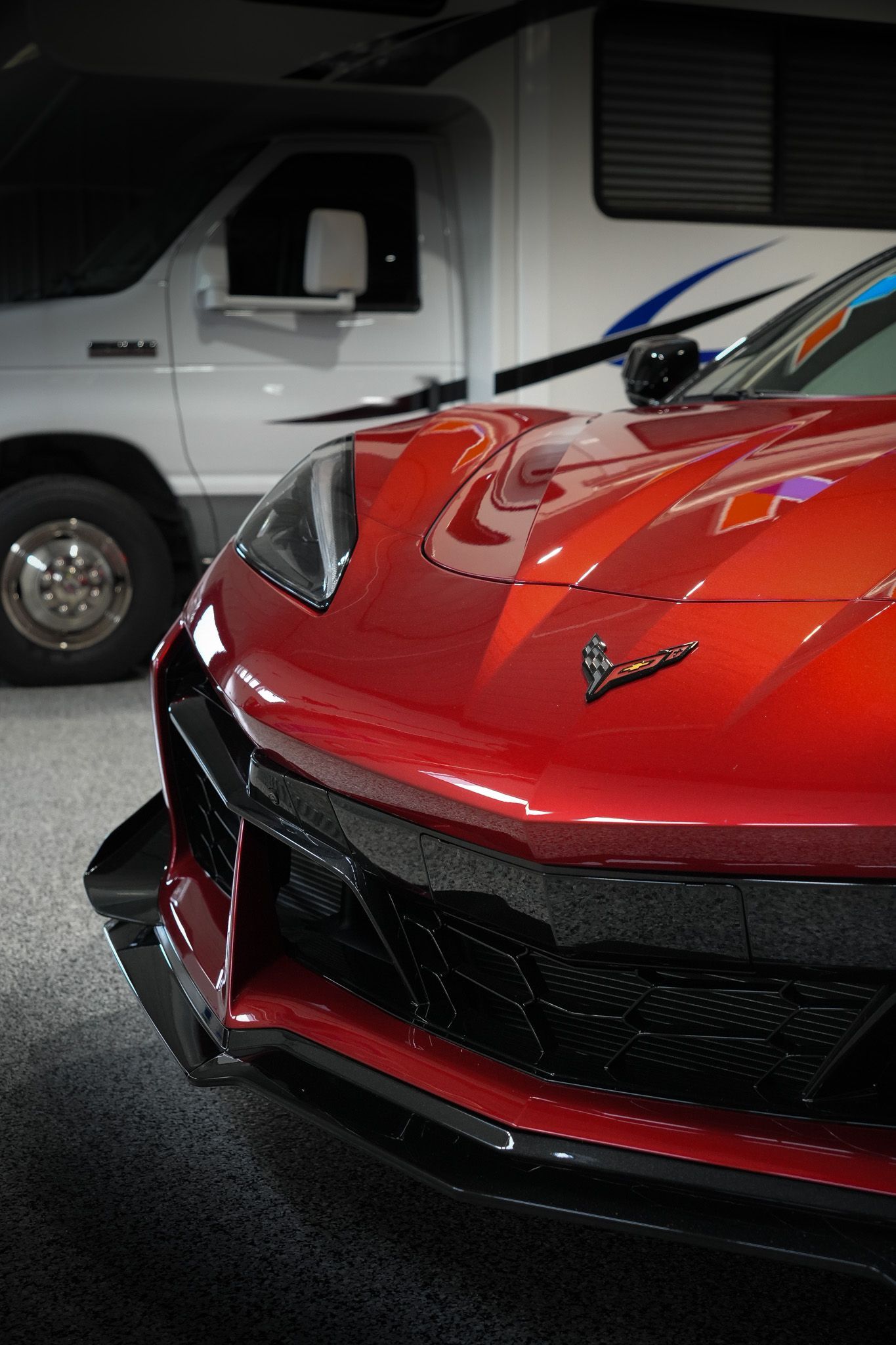A red sports car is parked in a garage next to a white van
