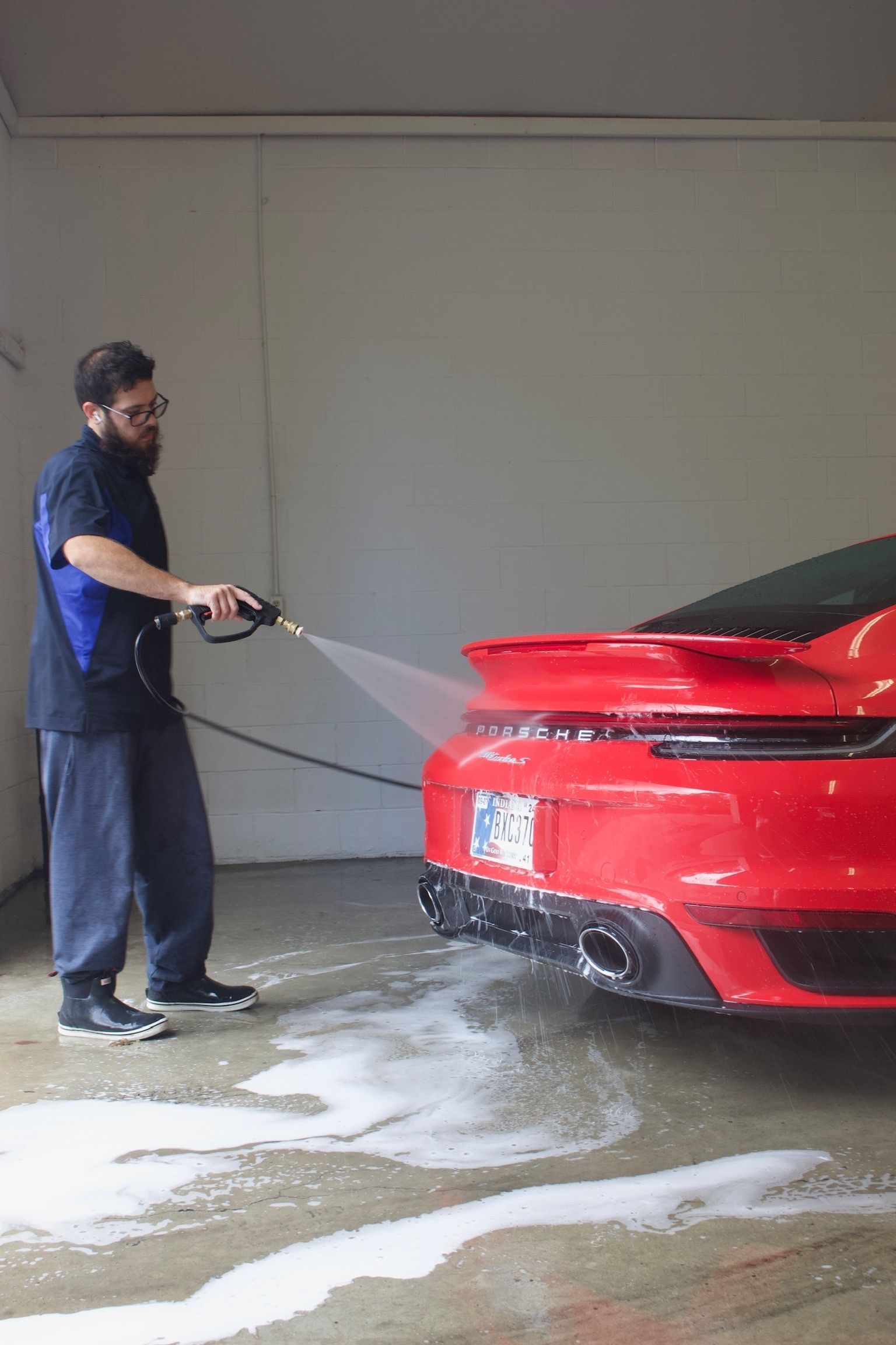 A man is cleaning the side mirror of a black car in a garage.