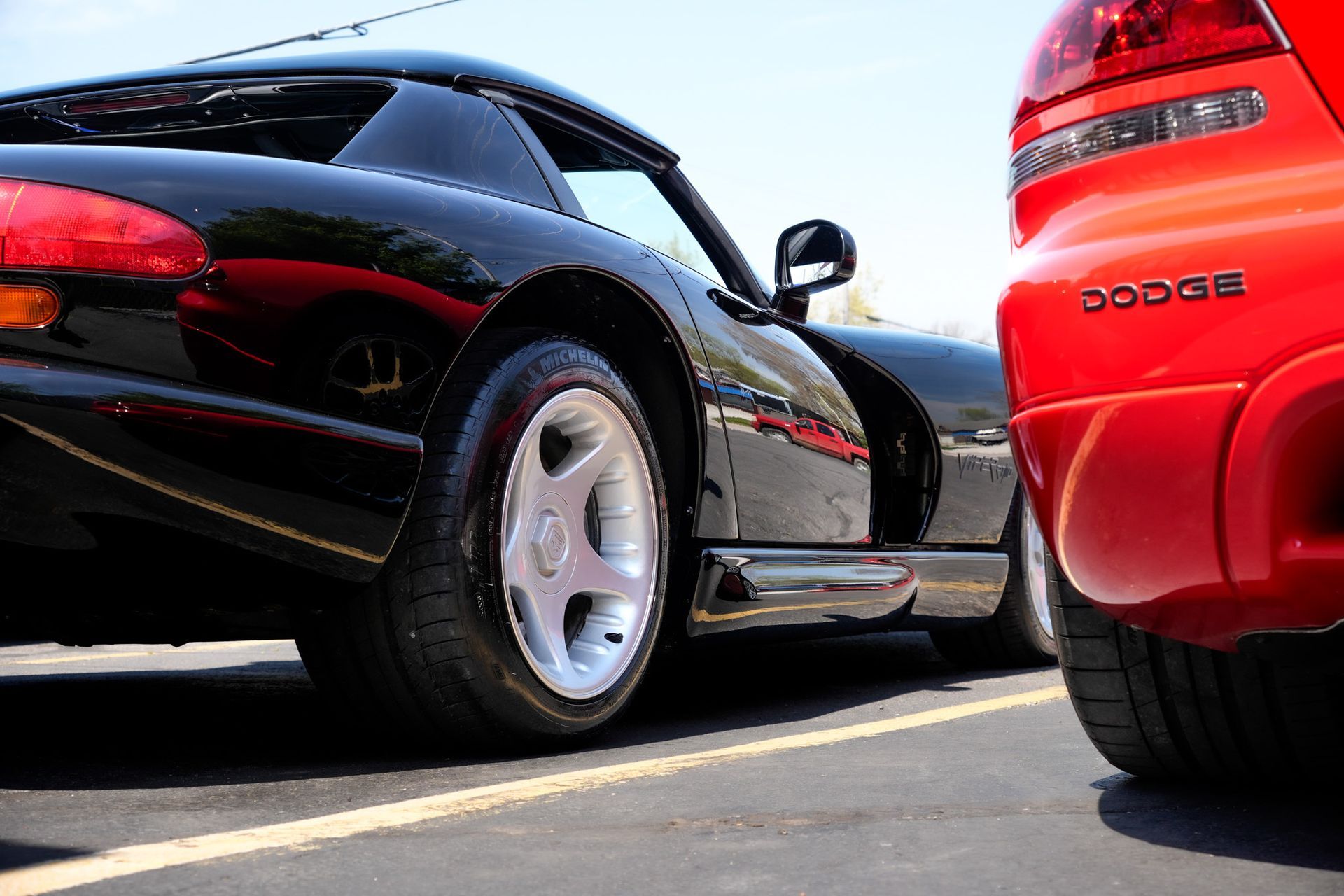Black Dodge Viper sports car parked next to a red Dodge car, on a paved lot.