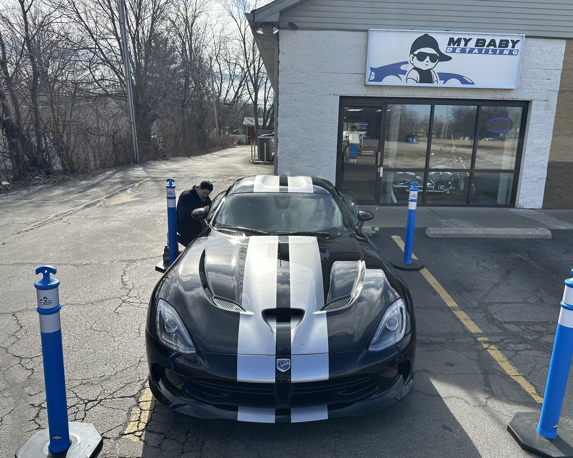 Black Dodge Viper with white stripes parked in front of a building, person nearby.