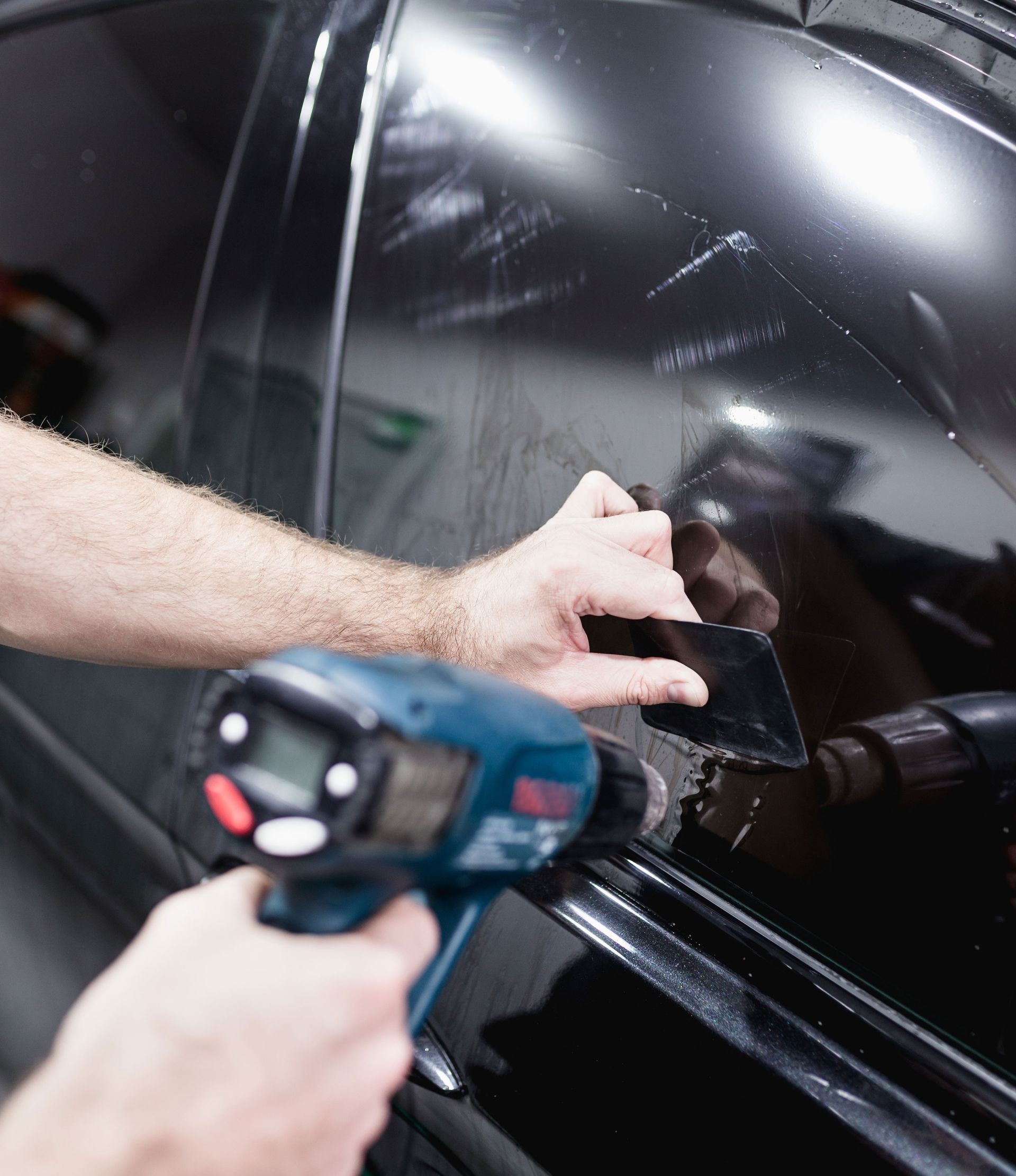 A person is applying tinted glass to a car window.