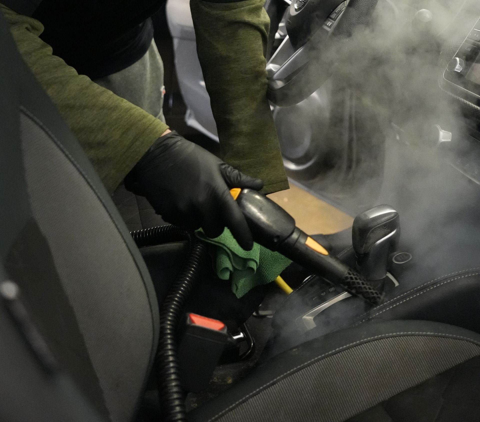 A man in a protective suit is cleaning the interior of a car.