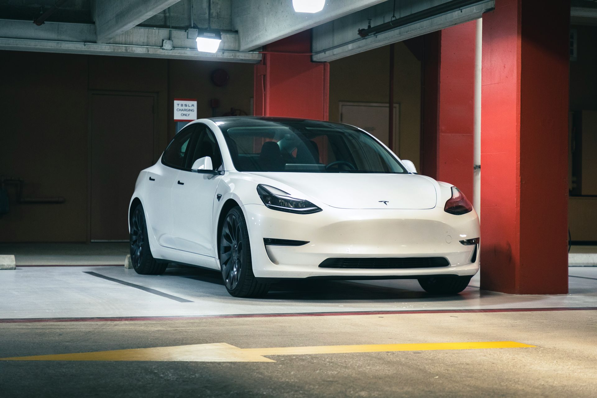A white tesla model 3 is parked in a parking garage.