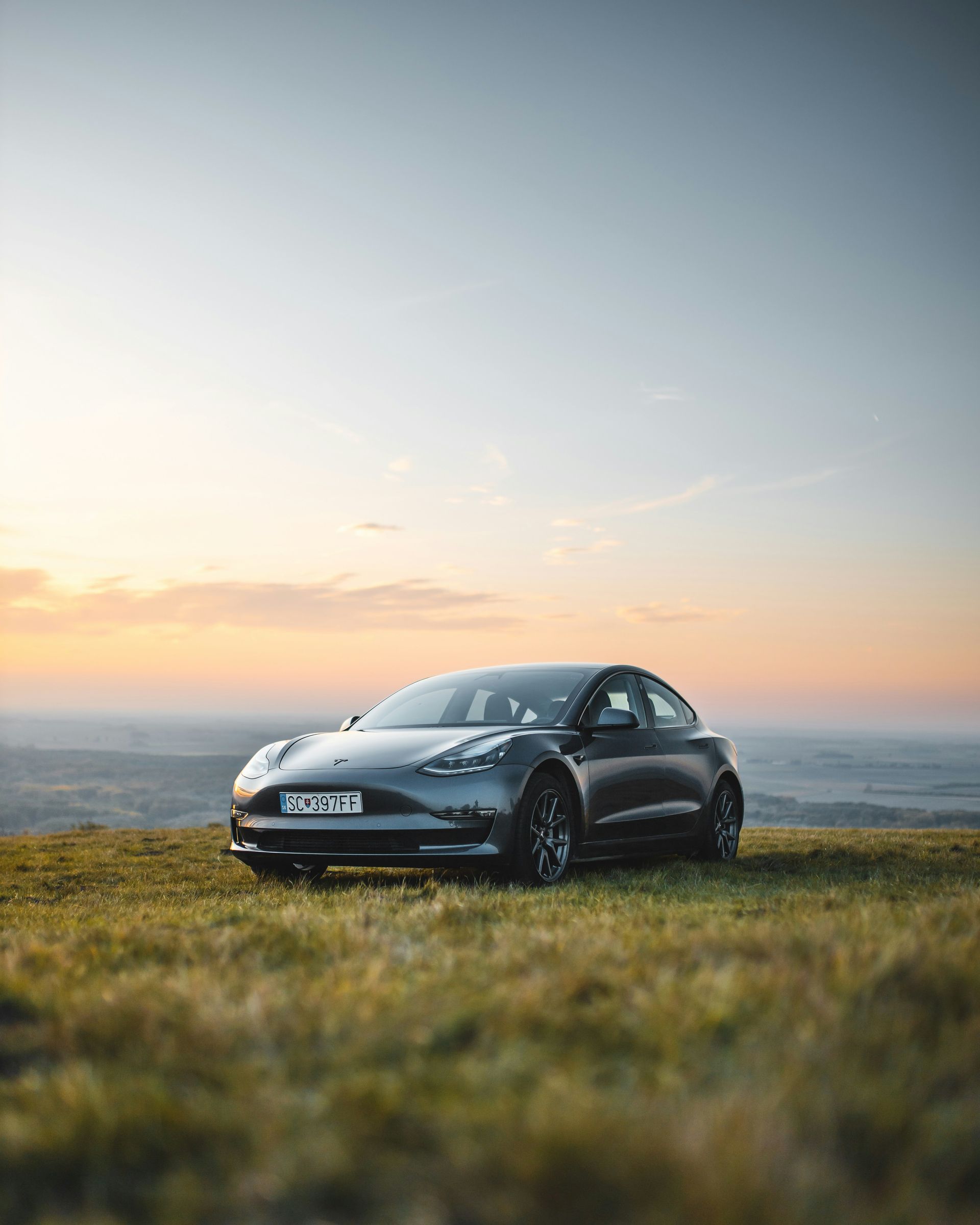 A tesla model 3 is parked on top of a grassy hill.