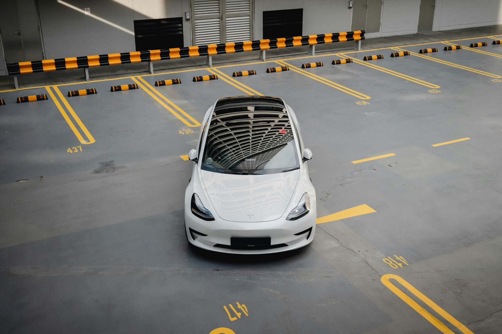 A white tesla model 3 is parked in a parking garage.