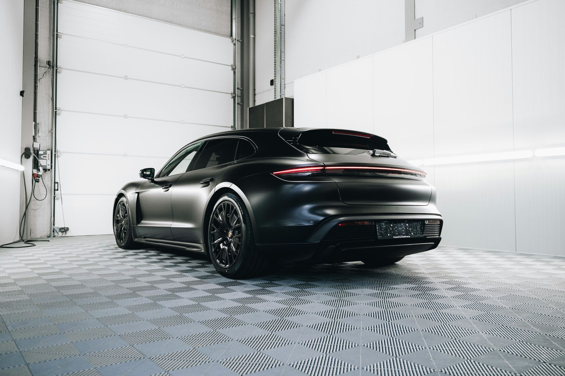 A black porsche taycan turbo s is parked in a garage.