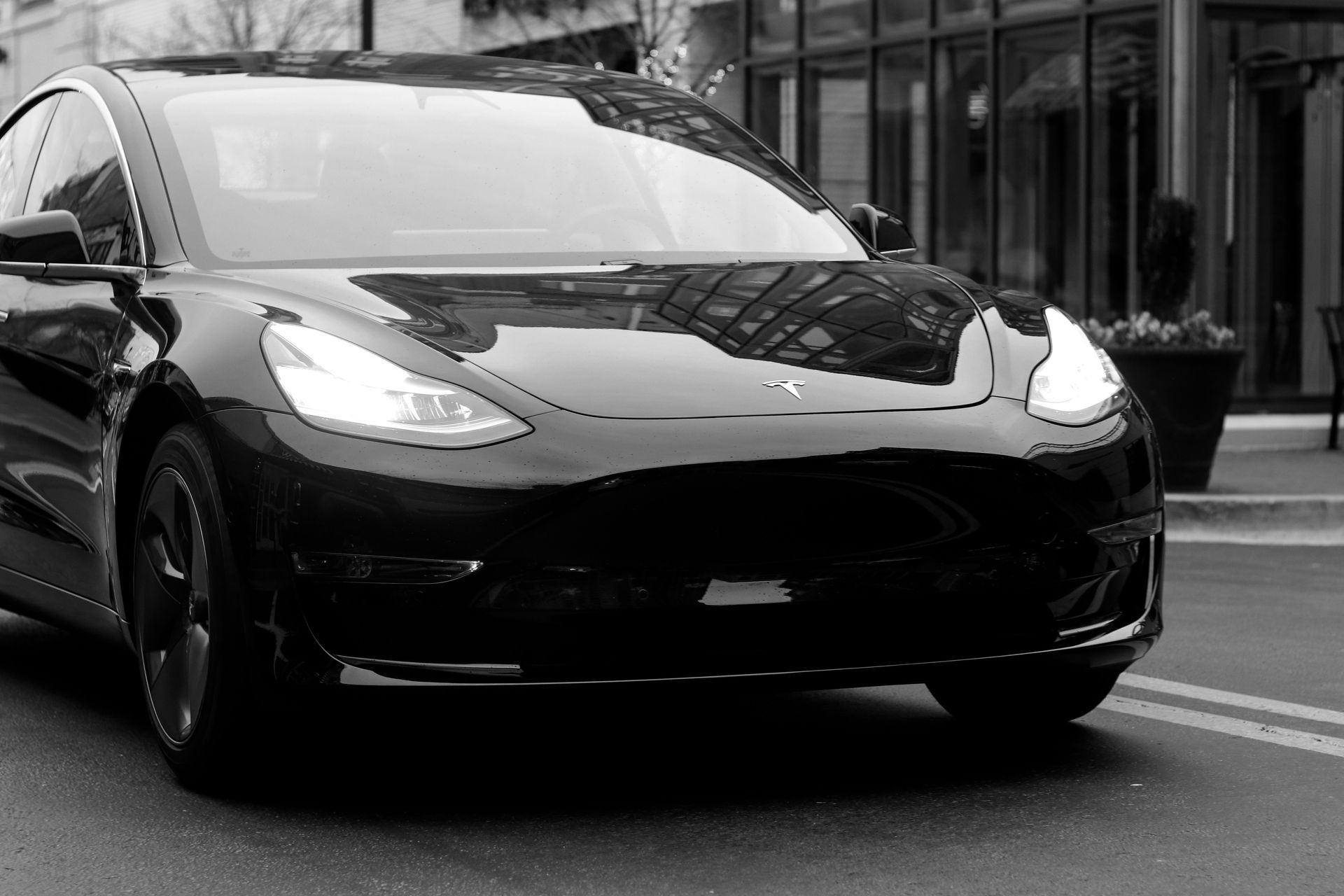 A black and white photo of a tesla model 3 driving down a city street.