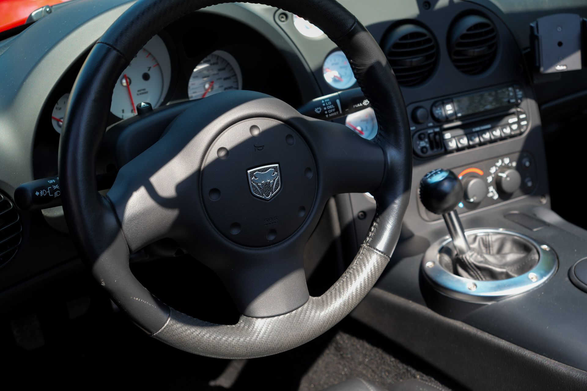 Black steering wheel with Dodge logo in a car's interior; manual gear shift visible.