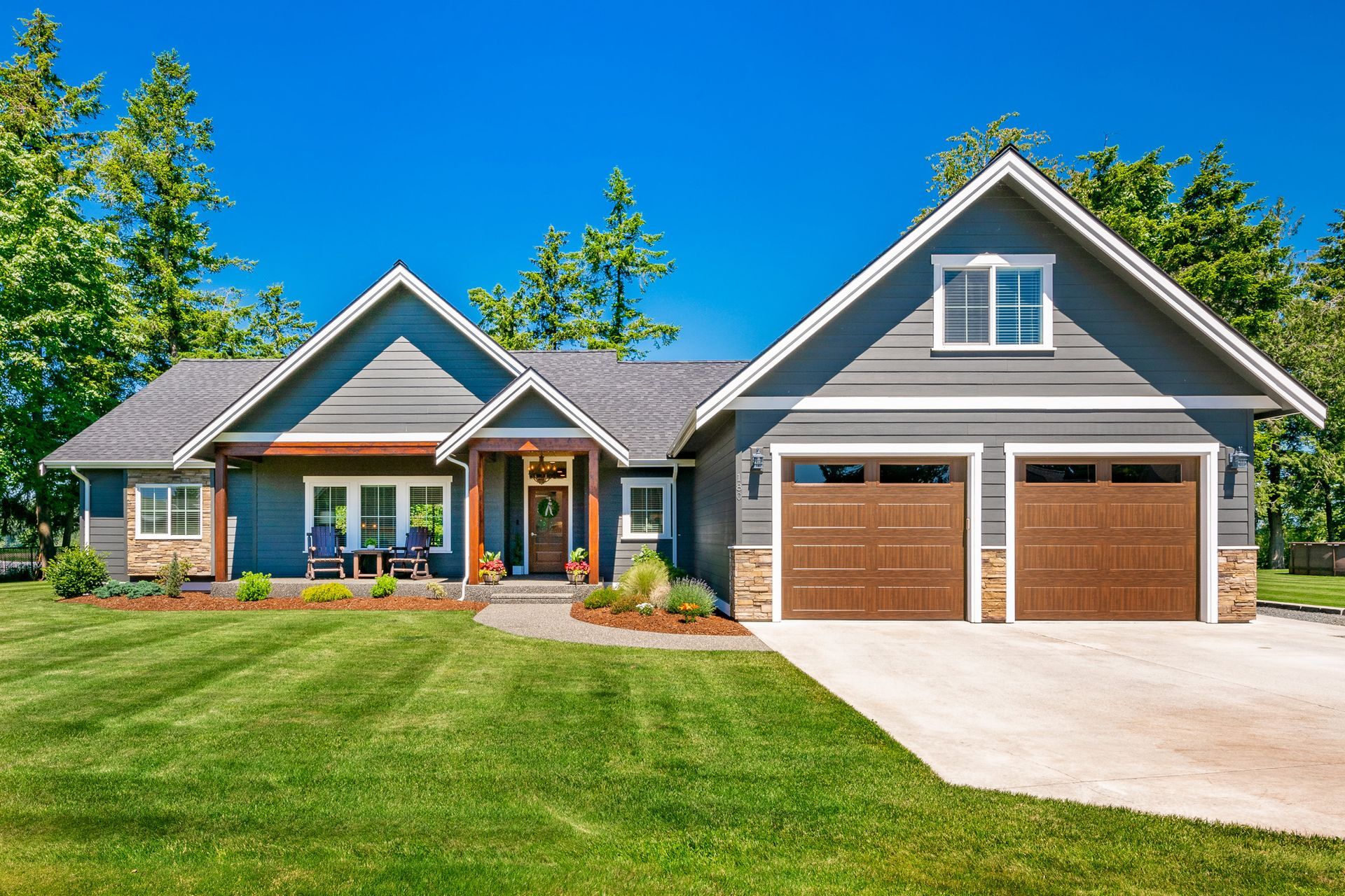 Gray house with brown garage doors and a green lawn under a blue sky.