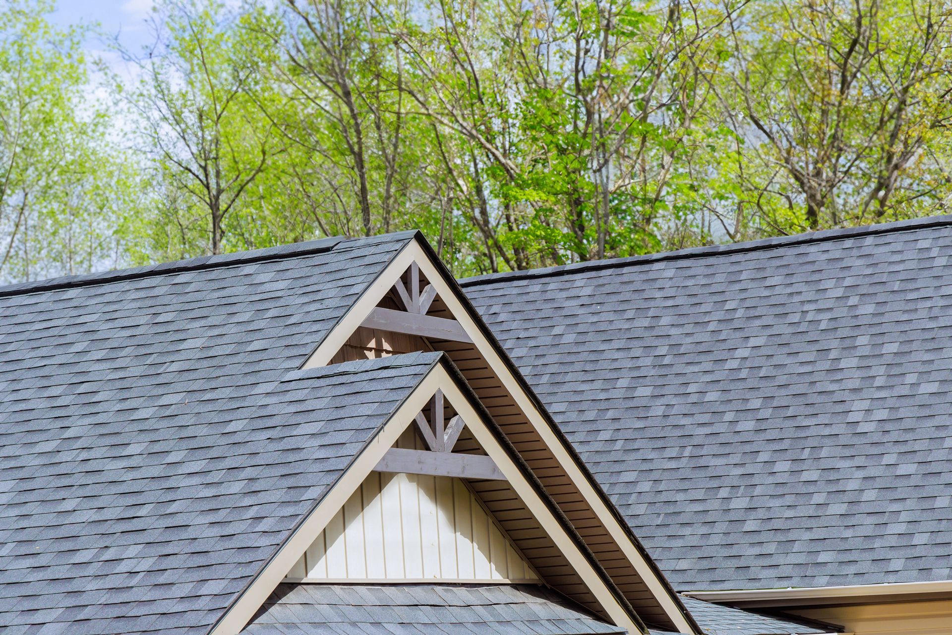 Gray shingled roof with two triangular dormers, trees in the background.