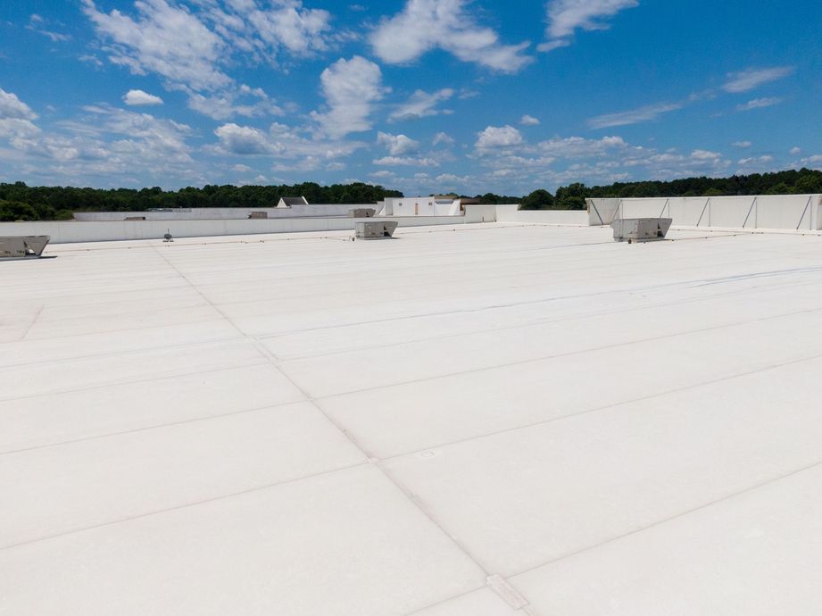 White commercial roof with air conditioning units, blue sky, and distant trees.