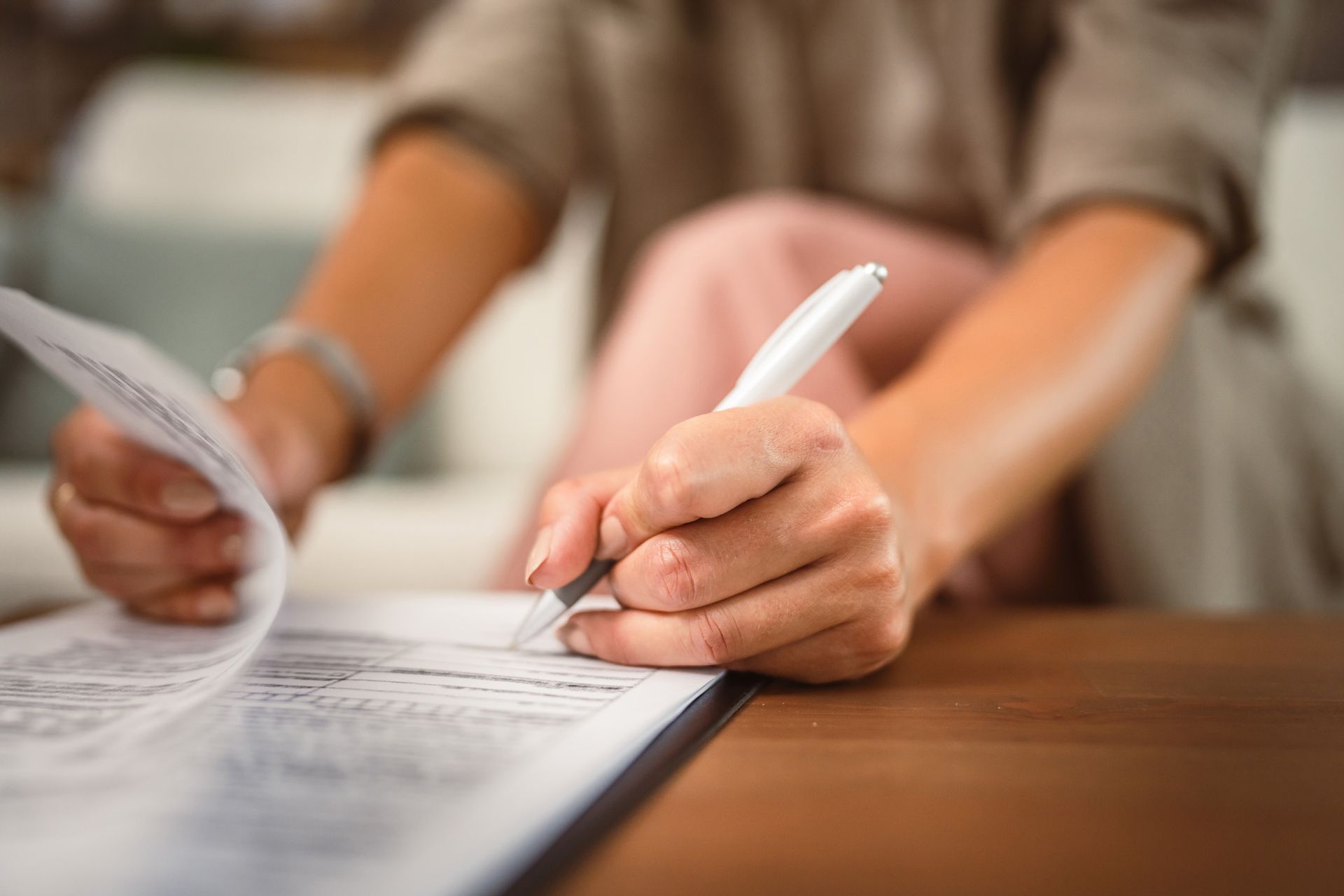 Woman's hands signing a document with a white pen on a table.