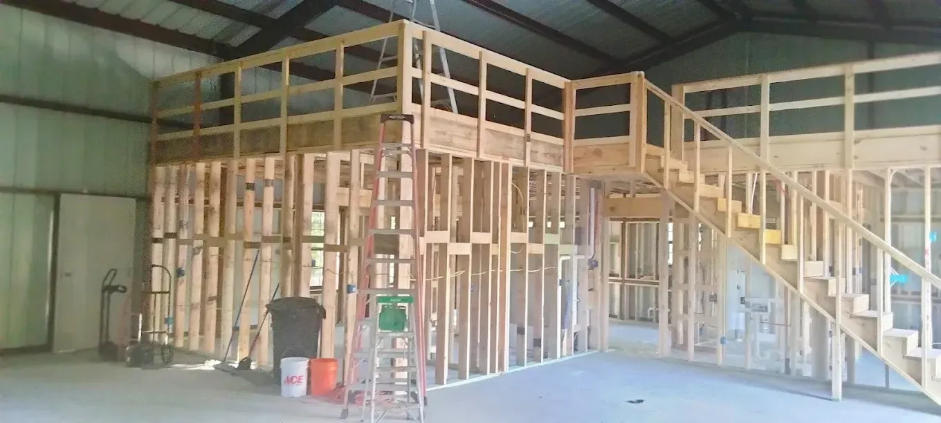 Interior view of a building under construction, featuring exposed wooden wall framing, a mezzanine level, and a staircase.