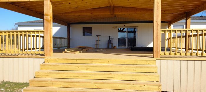 A covered wooden deck with a staircase leading up to a house exterior featuring a glass sliding door and light siding.