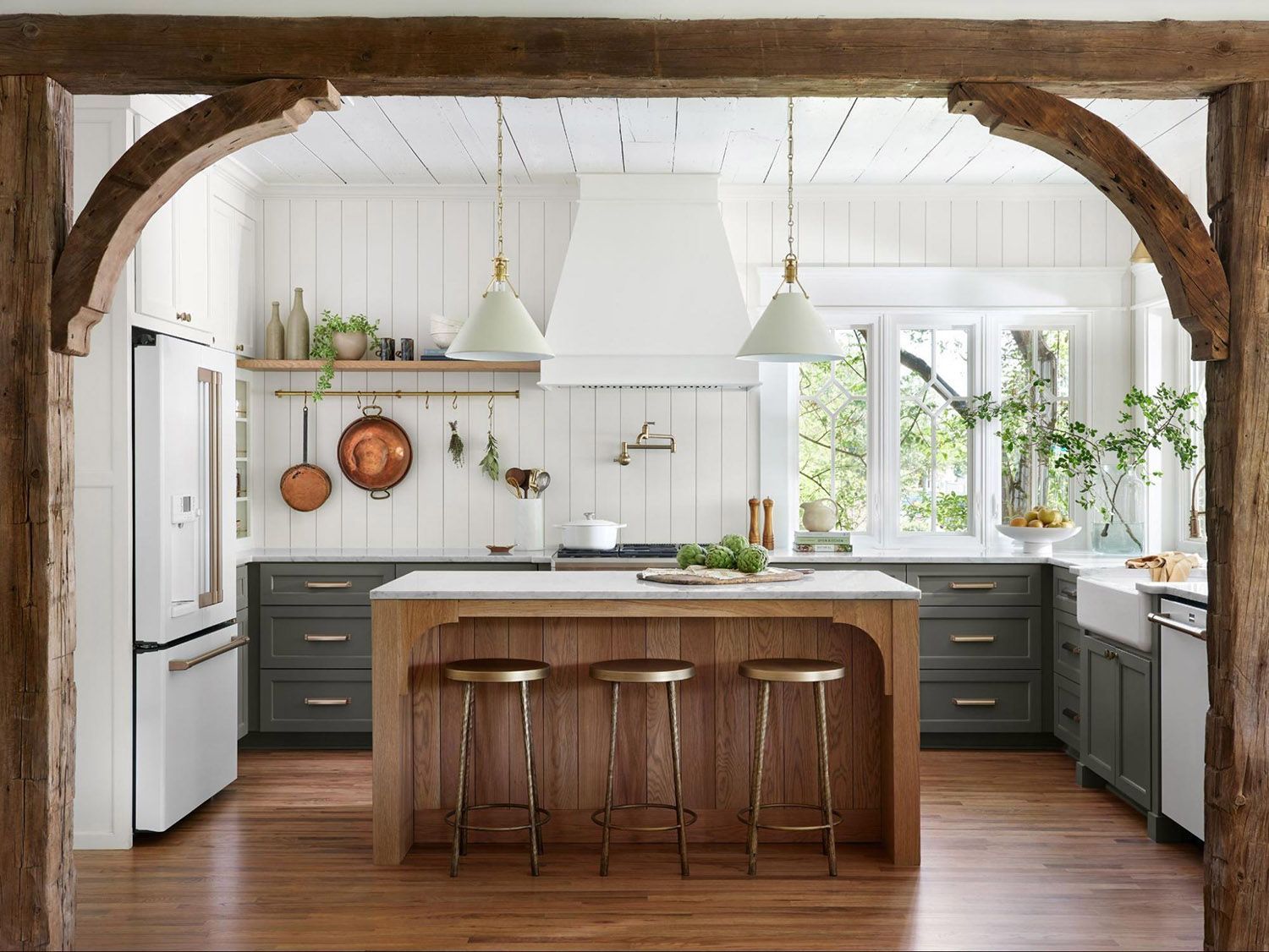 A bright, modern farmhouse kitchen featuring dark grey cabinets, a wooden island with three stools, and white walls.