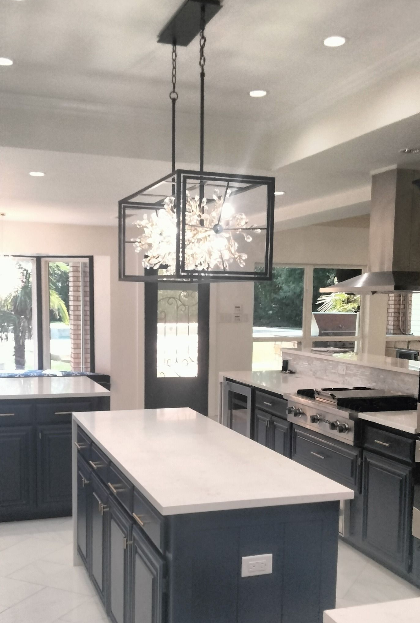 A modern kitchen with navy blue cabinetry, white countertops, and a rectangular, crystal-filled black pendant light.