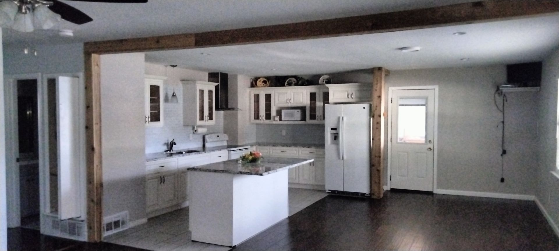 A kitchen with white cabinets, a central island, and wood-framed open concept views, featuring dark hardwood flooring.
