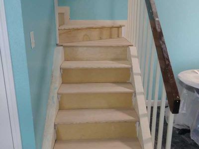 Unfinished wooden staircase ascending between light blue walls, with a partial railing on the right side.
