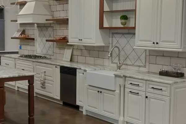 A kitchen with white cabinets, a farmhouse sink, marble-style countertops, open wood shelving, and white subway tile walls.