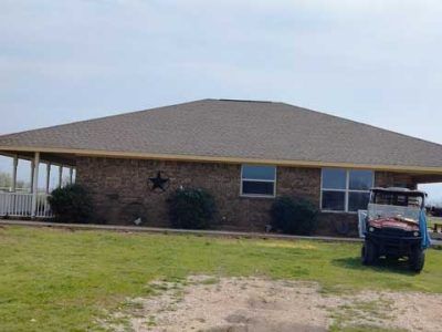 A brick house with a hip roof and a wrap-around porch, featuring a black star wall ornament and a parked utility vehicle.