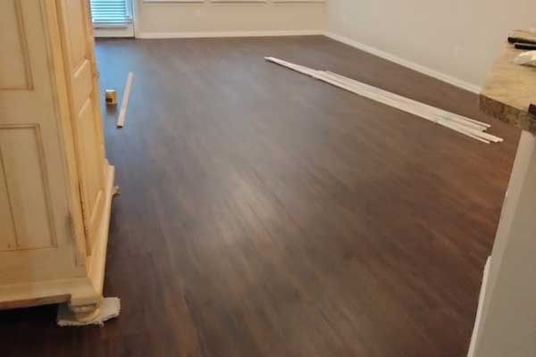 A room with newly installed dark wood-look plank flooring, featuring trim pieces lying on the floor and a wooden cabinet.