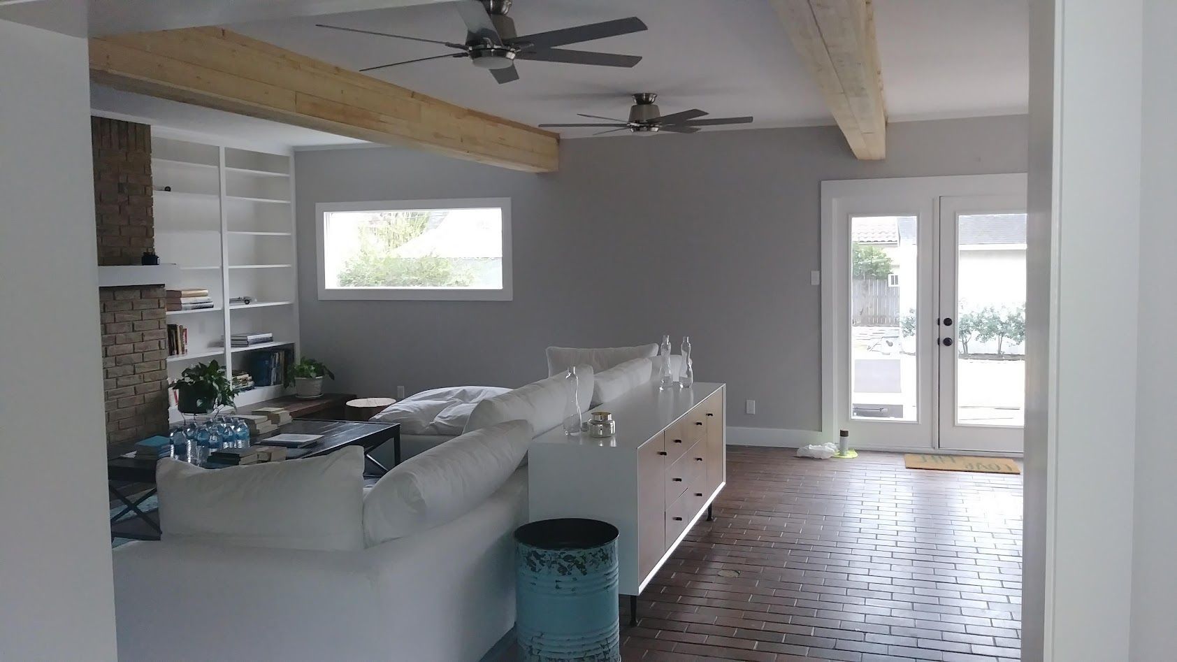 A living room with a white sofa, a long white console table, two ceiling fans, and glass doors opening to a yard.