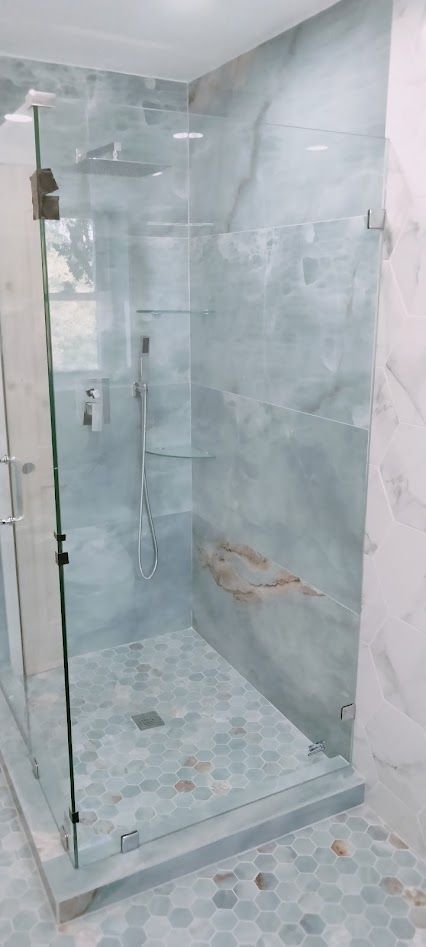 A walk-in shower with light blue marble walls, a glass door, and a pebble-stone tile floor in a modern bathroom.