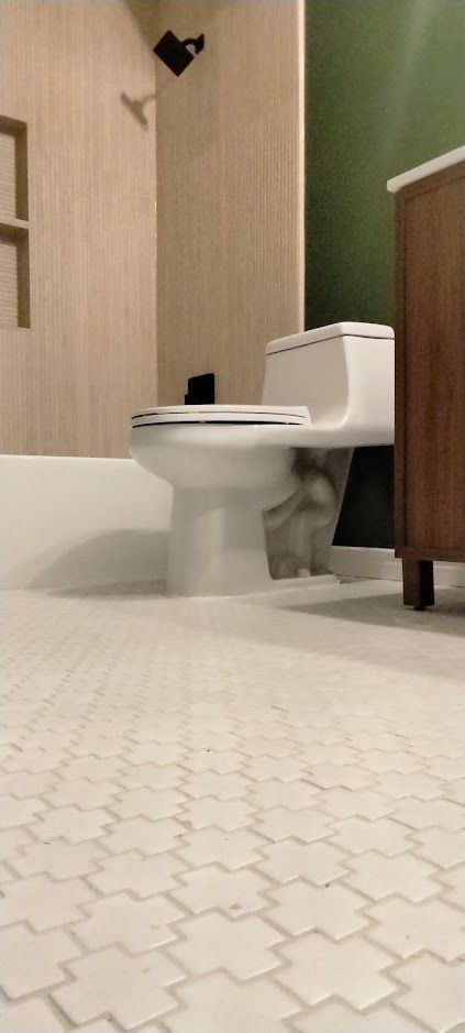 A view from the floor in a modern bathroom featuring light-toned tile, a white toilet, and a wooden vanity.