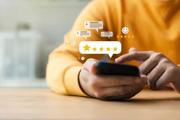 A person in a yellow long-sleeved shirt holds a smartphone, interacting with digital five-star review and chat icons.