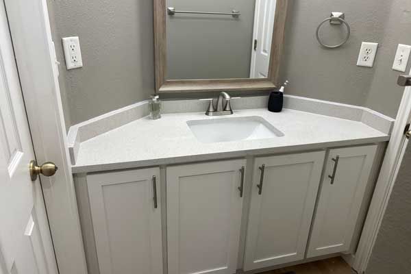 Corner bathroom vanity with white cabinets, a light-colored countertop, an undermount sink, and a rectangular mirror.