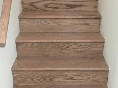 A set of four wooden stairs viewed from above, featuring a light brown, natural wood grain finish between two white walls.