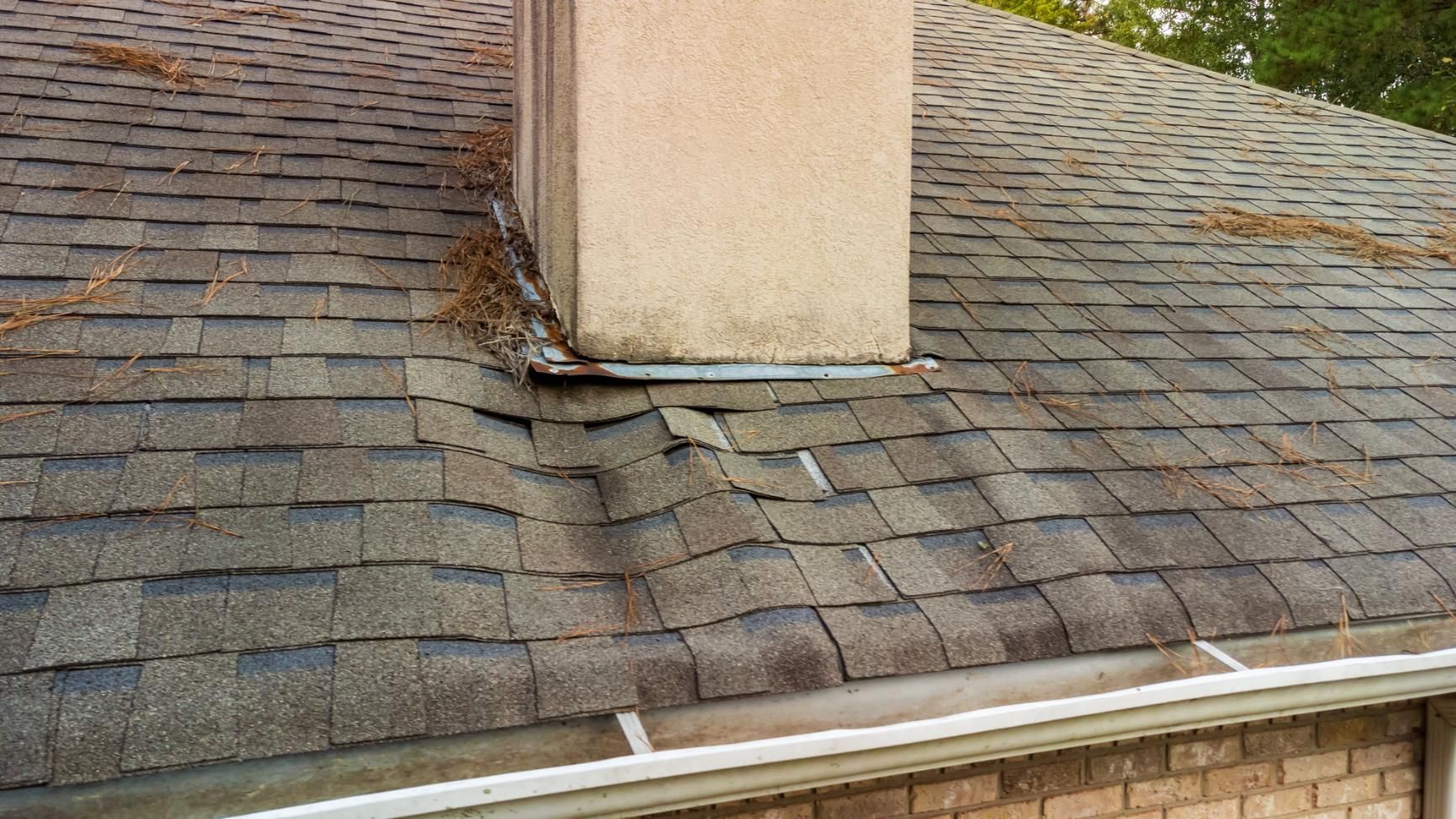 Roof with chimney, visible buckling near the chimney base, with debris and gutter in the view.