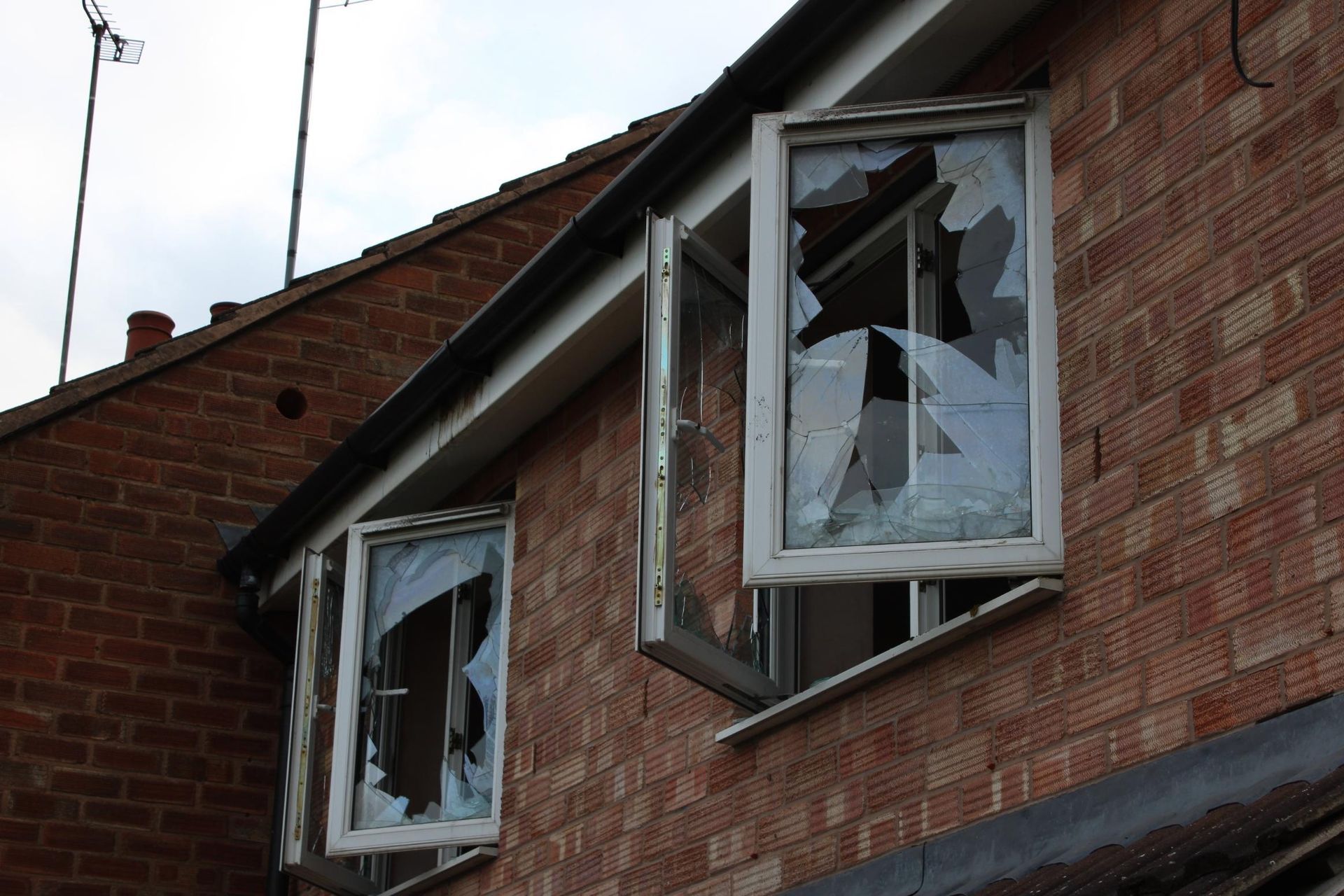 Two broken windows on a brick building with an open window frame, overcast sky.