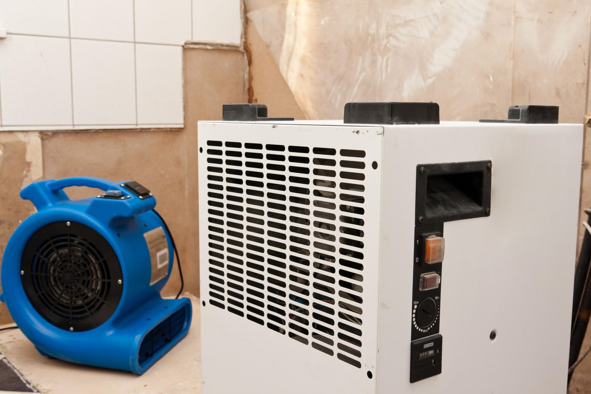 Blue fan and large white dehumidifier in a room with exposed wall.