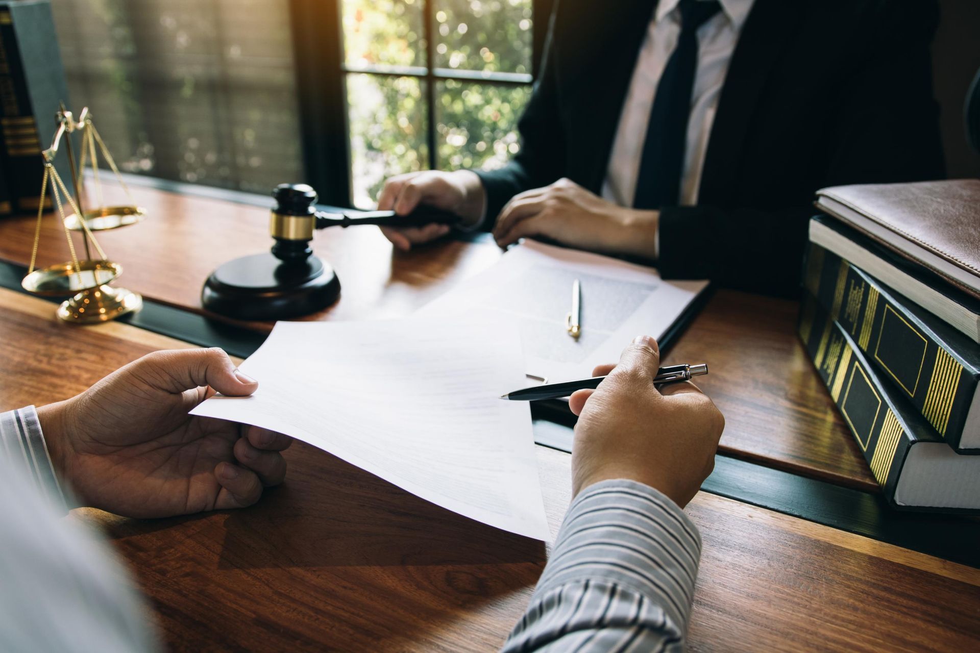 Person signing legal documents at a lawyer's office, with gavel and law books present.