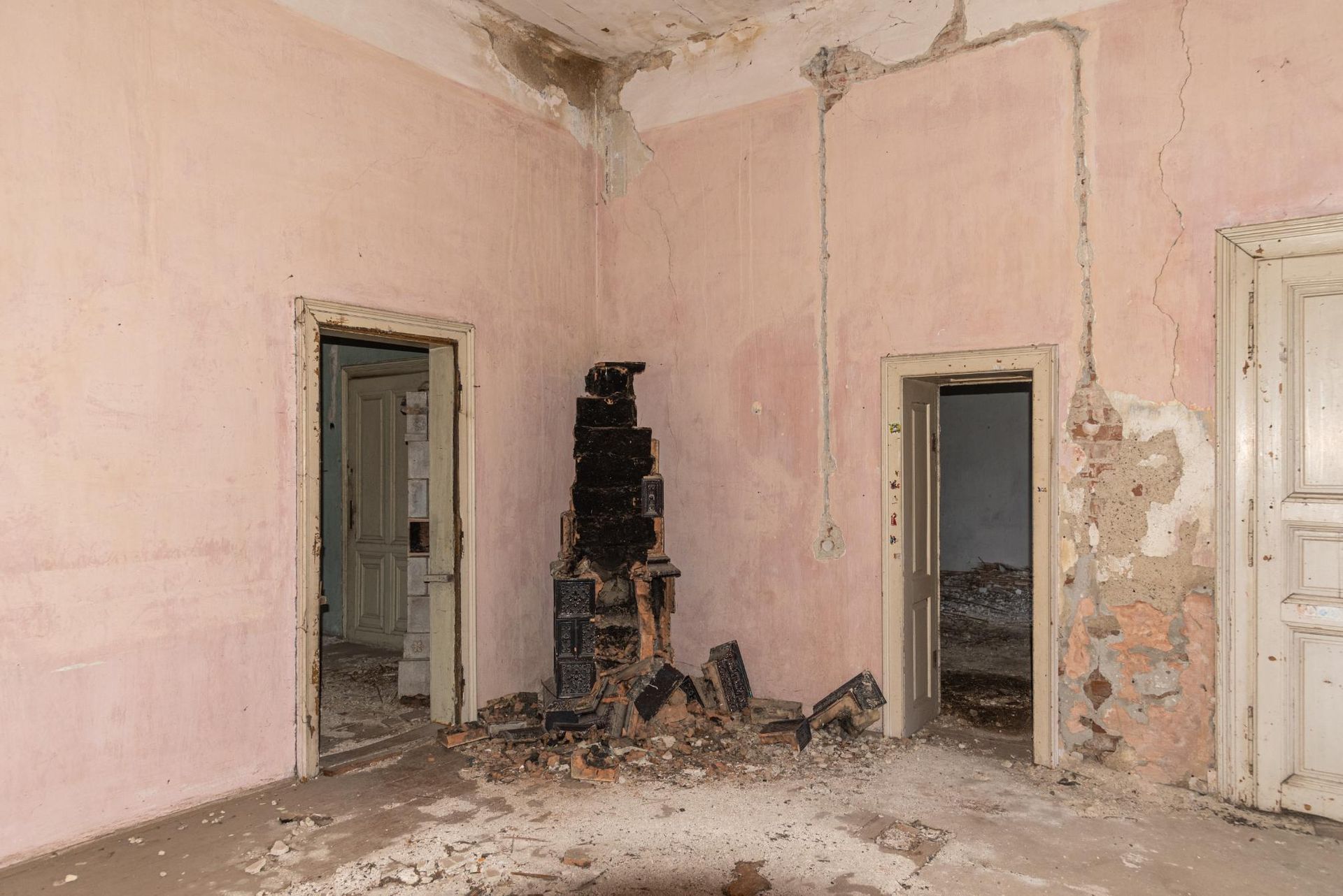 Dilapidated room with pink walls, two doorways, and a charred fireplace. Debris litters the floor.