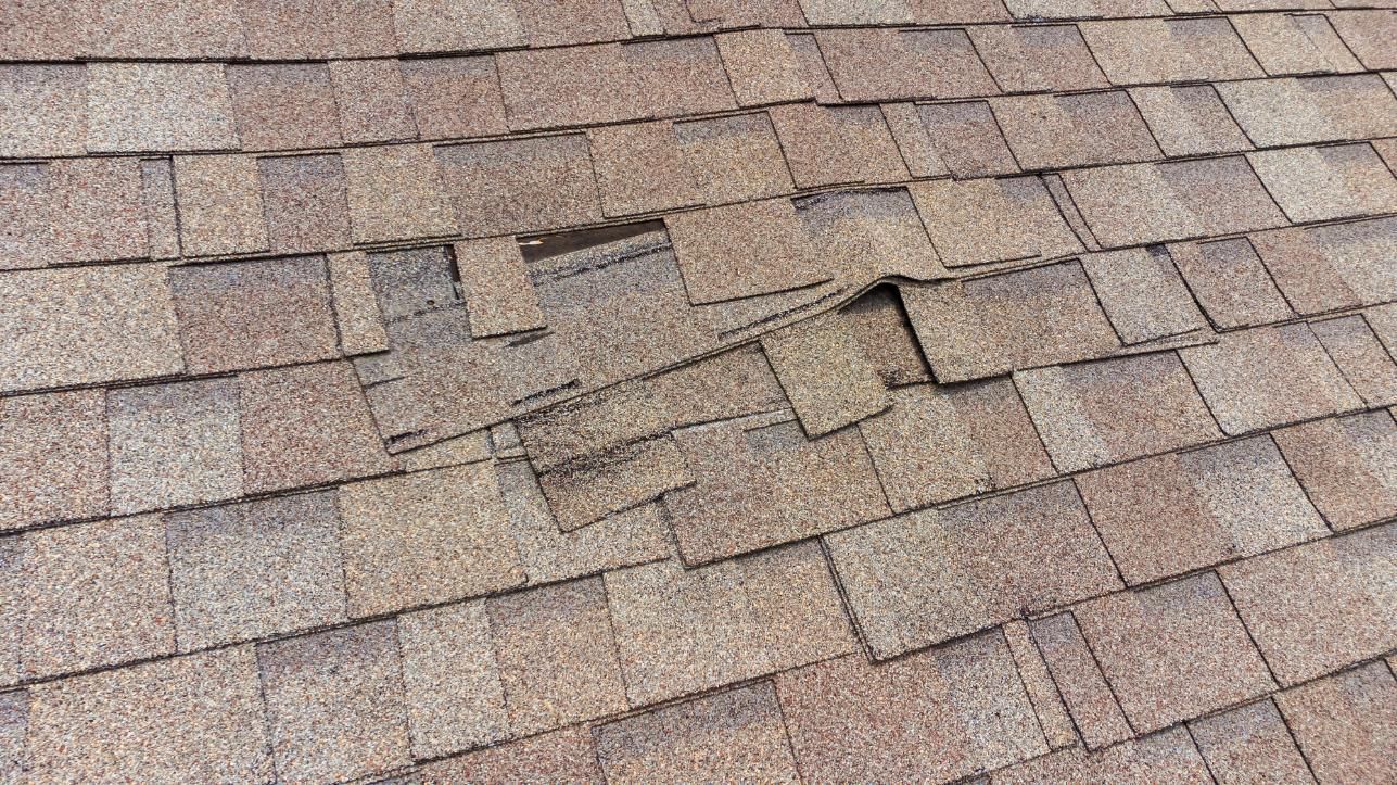 Damaged asphalt shingle roof. Several shingles are missing or broken, exposing the underlying material.