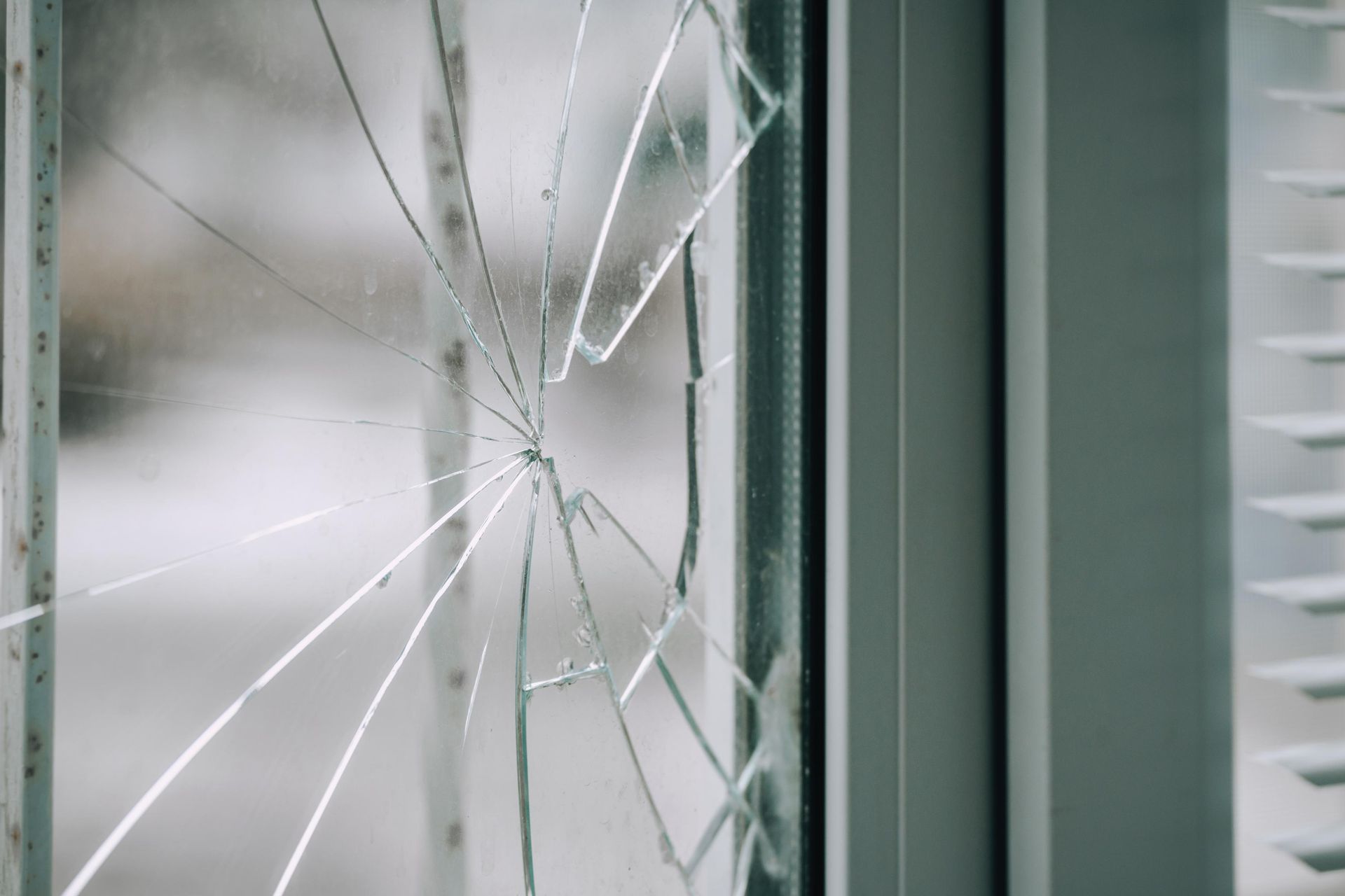 Cracked window pane with visible cracks radiating outward. Blurred outdoor background.
