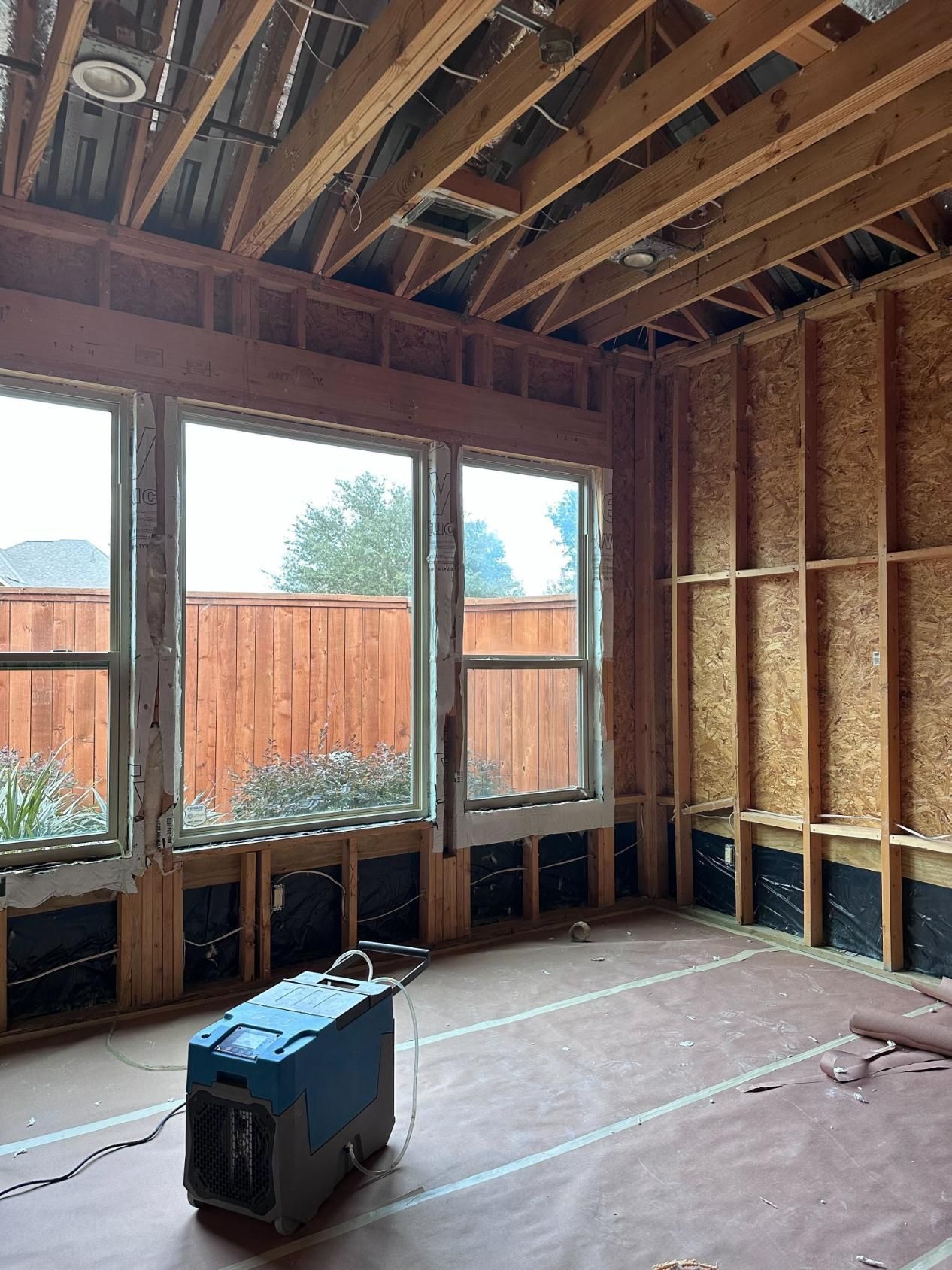 Room under construction with exposed wood framing, windows, and a dehumidifier on the floor.