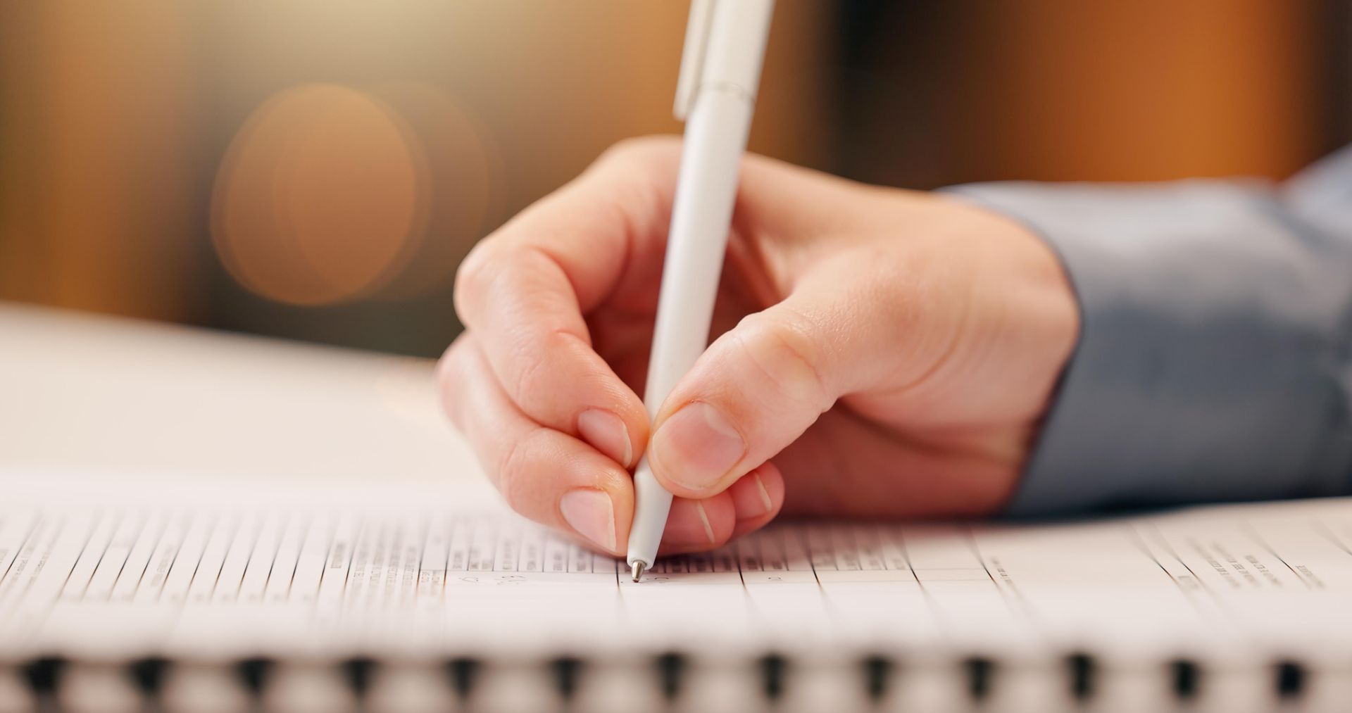 Hand with white pen writing on a notebook, close-up.