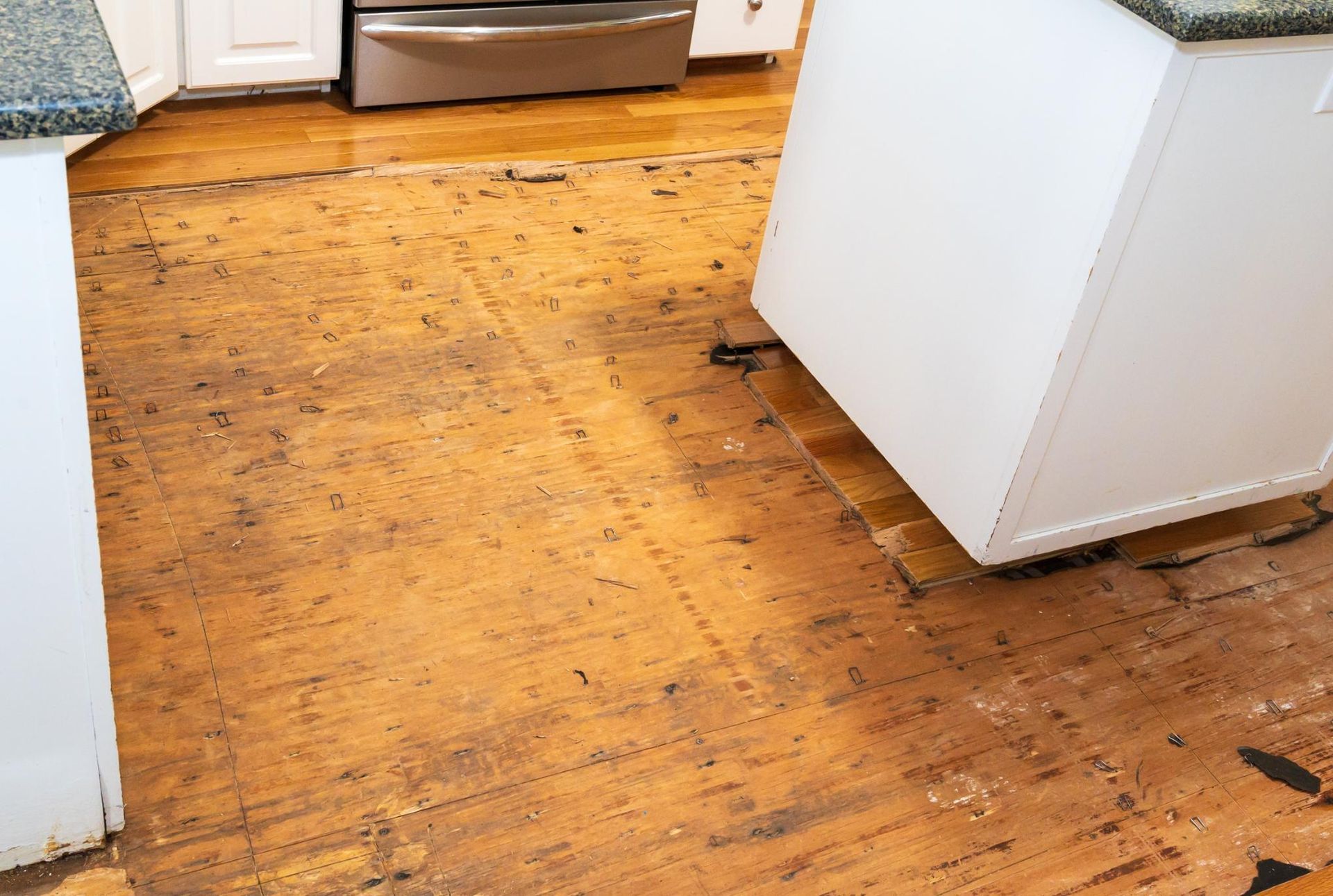 Exposed hardwood floor with kitchen cabinets in the process of renovation.