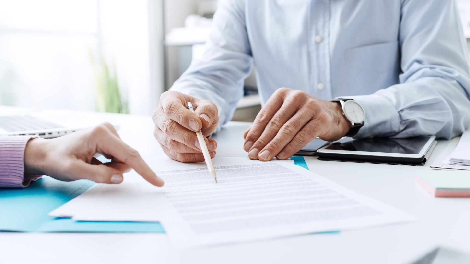 Two people reviewing paperwork at a desk, one pointing with a pencil, the other with a finger.
