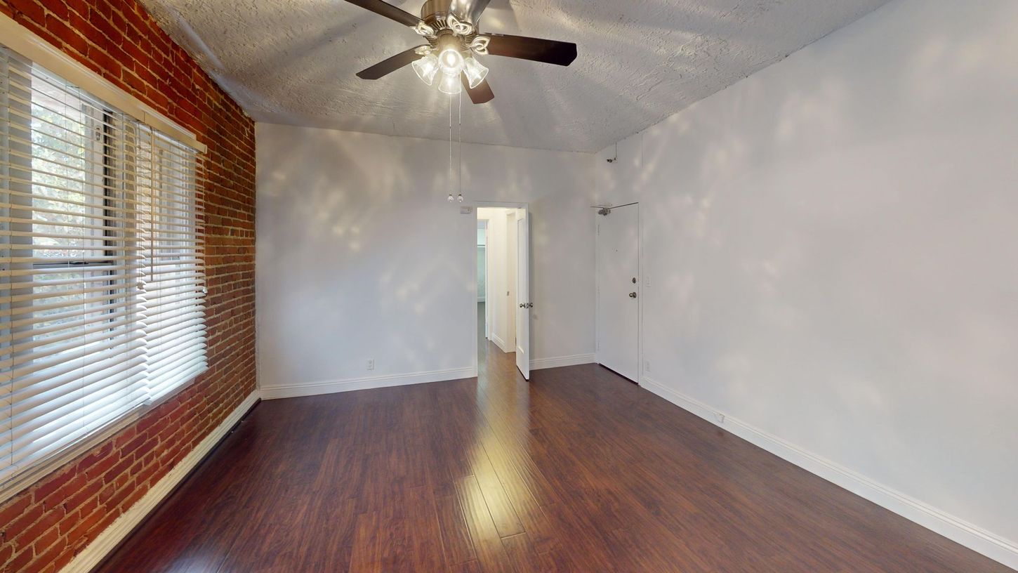 Empty room with wood floors, brick wall, and a ceiling fan.