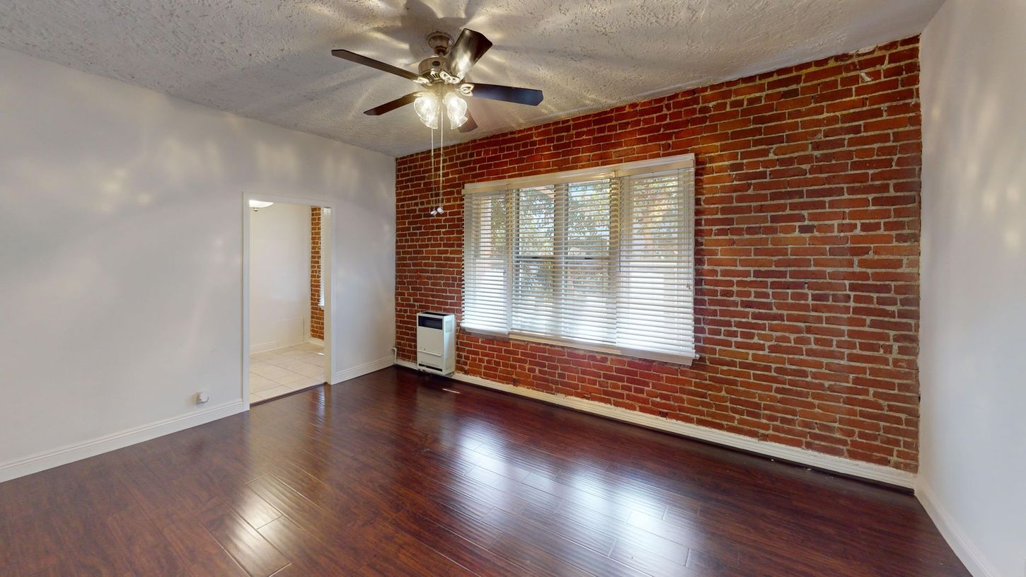 Empty room with exposed brick wall, window, and wood floor.