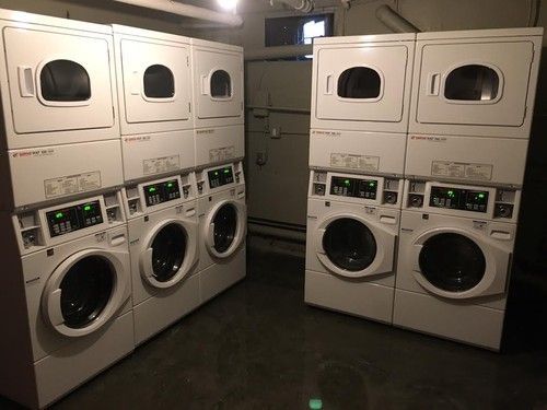 White laundry machines in a dimly lit room, stacked in pairs.