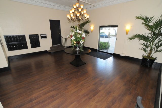 Elegant building lobby with dark wood floors, chandelier, and floral arrangement.