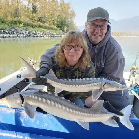 A man and a woman are holding two sturgeon on a boat.